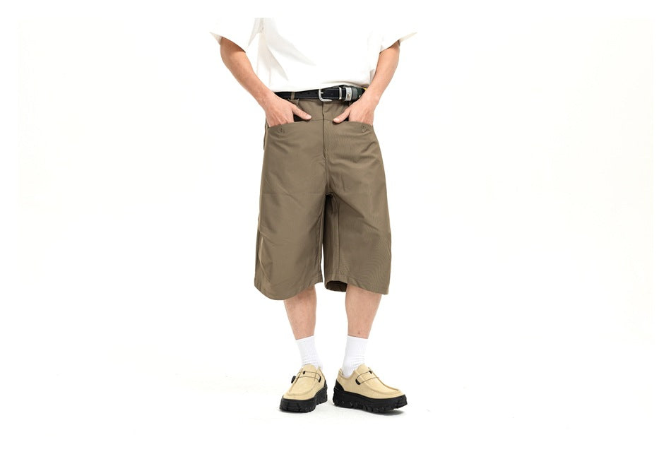 Front view cropped at the shoulders of a model wearing loose olive-brown knee-length shorts and beige shoes.