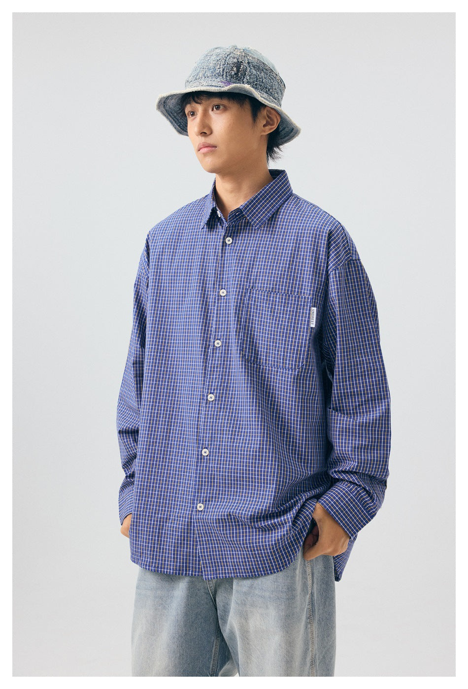 Front view of a model in a blue checked button-up shirt with a chest pocket and white buttons.