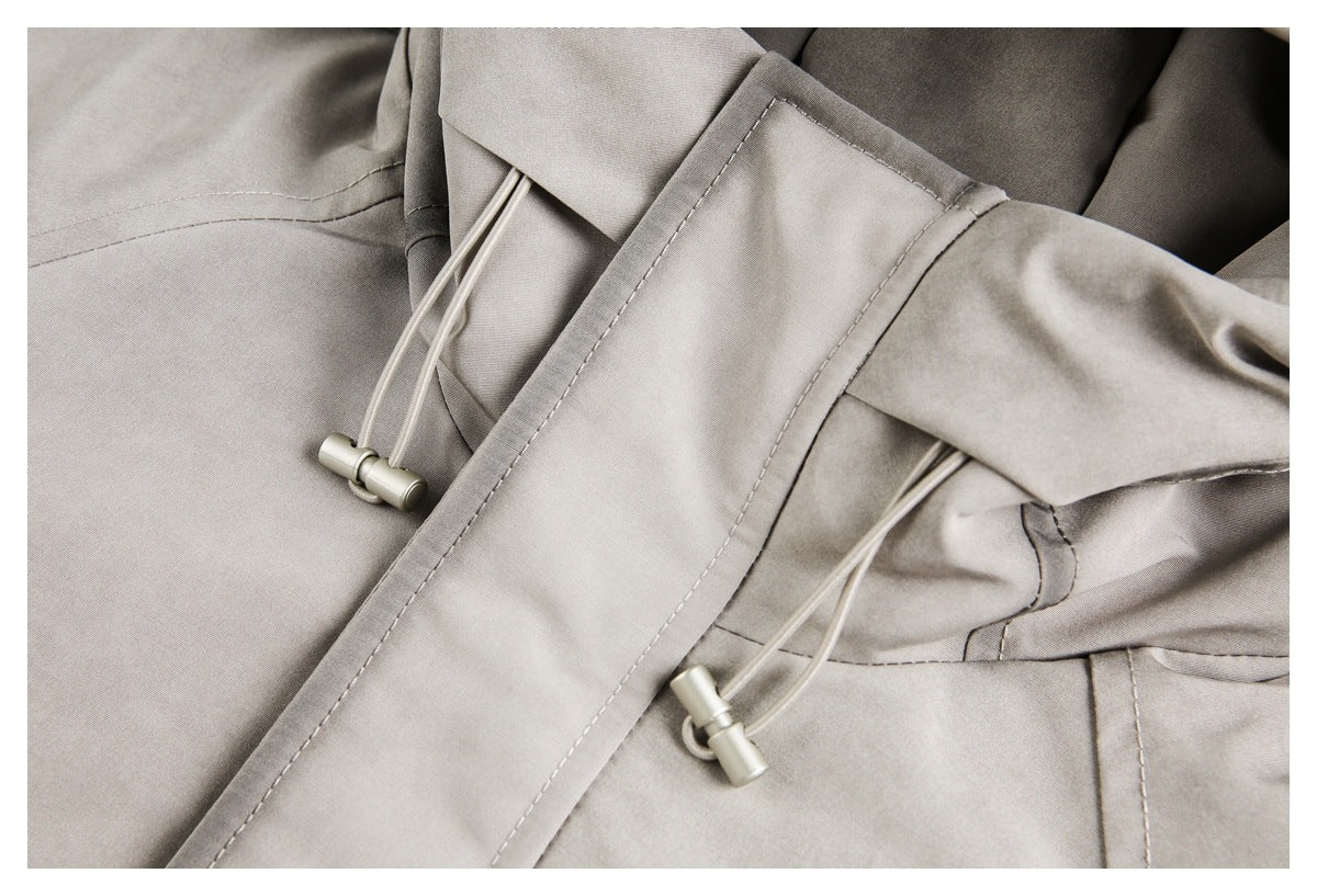 Close-up of light gray jacket drawcords, metal toggles, stitched placket, and hood construction.