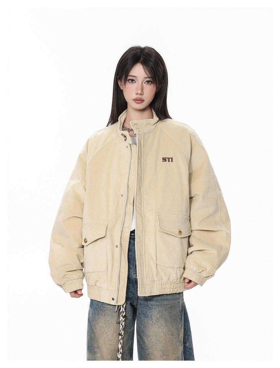 Front view of a model in a beige oversized jacket with snap-front closure, two flap pockets, and small chest embroidery.