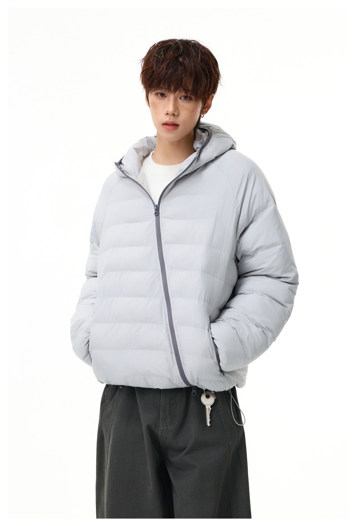 Model wearing a light gray hooded quilted jacket zipped diagonally, with a white top and dark pants