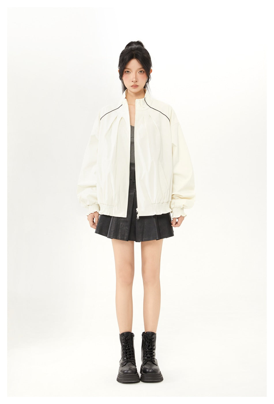 Model wearing an off-white zip jacket with black piping over a gray top, black pleated mini skirt and black boots