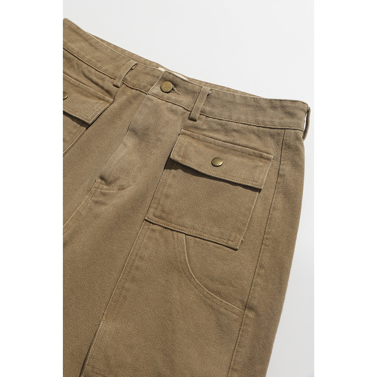 Close-up of tan shorts showing the waistband, button, belt loops, and large flap pocket with a brass-tone snap.