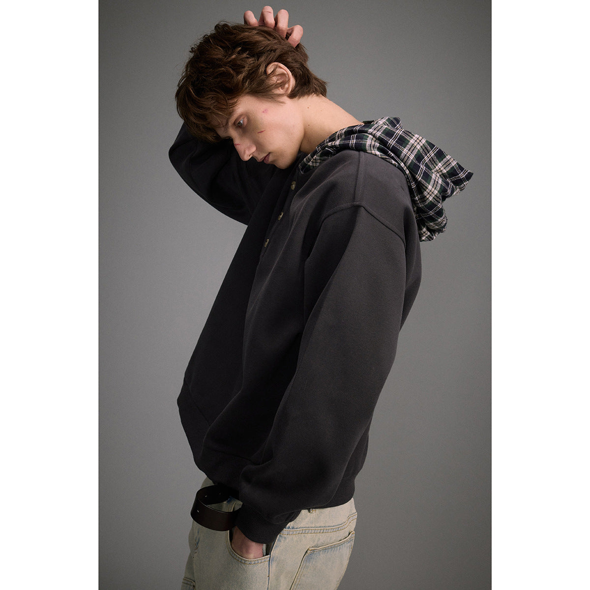 Side view of a man wearing a charcoal pullover with a black plaid-lined hood.