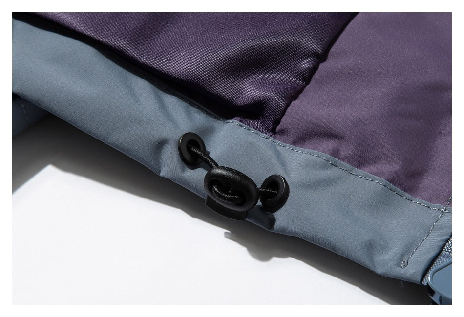 Close-up of a blue-gray garment edge with a black cord toggle beside a purple panel.