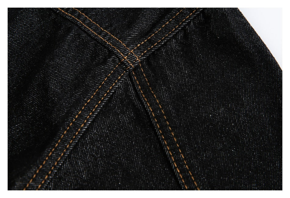 Close-up of intersecting seams on black denim with contrasting orange stitching.