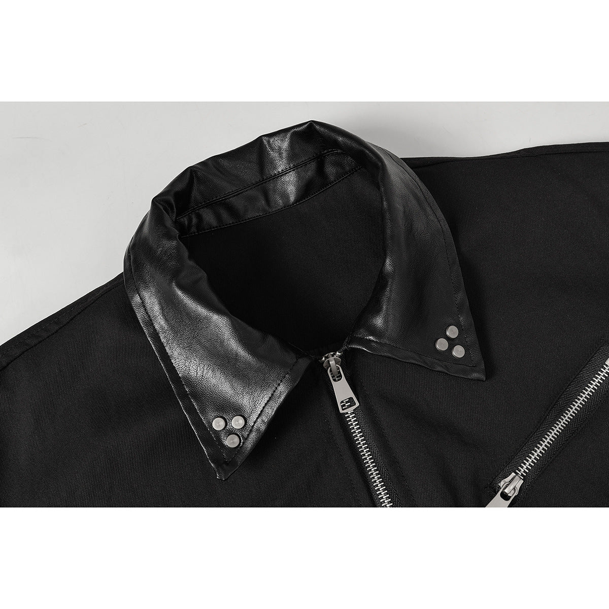 Close-up of a black jacket’s glossy leather-look pointed collar with silver snaps and front zippers.