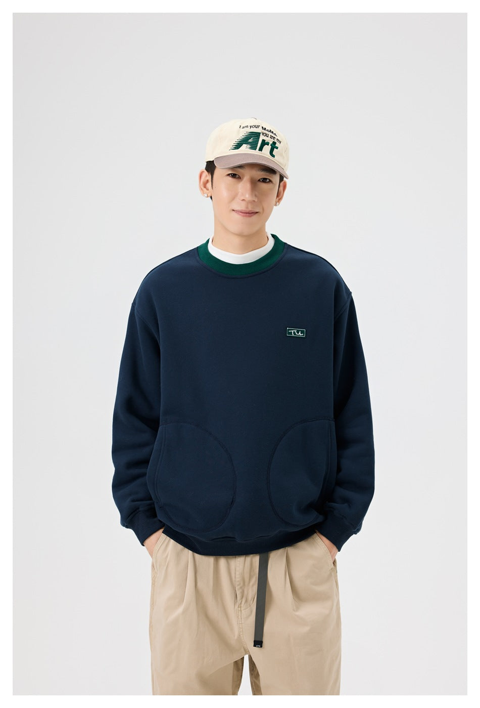 Close view of a model wearing a navy sweatshirt with green ribbed collar trim and two rounded front pockets.