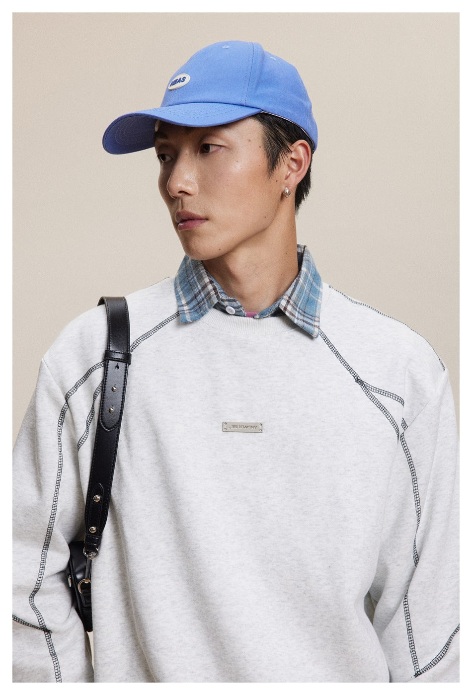 Close view of a model wearing a light gray sweatshirt with dark contrast seams and a small chest plaque.