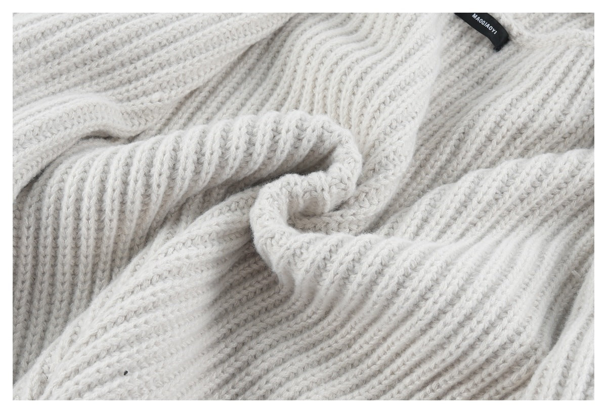 Close-up of off-white chunky ribbed knit fabric gathered in folds, with a small black label at the edge.