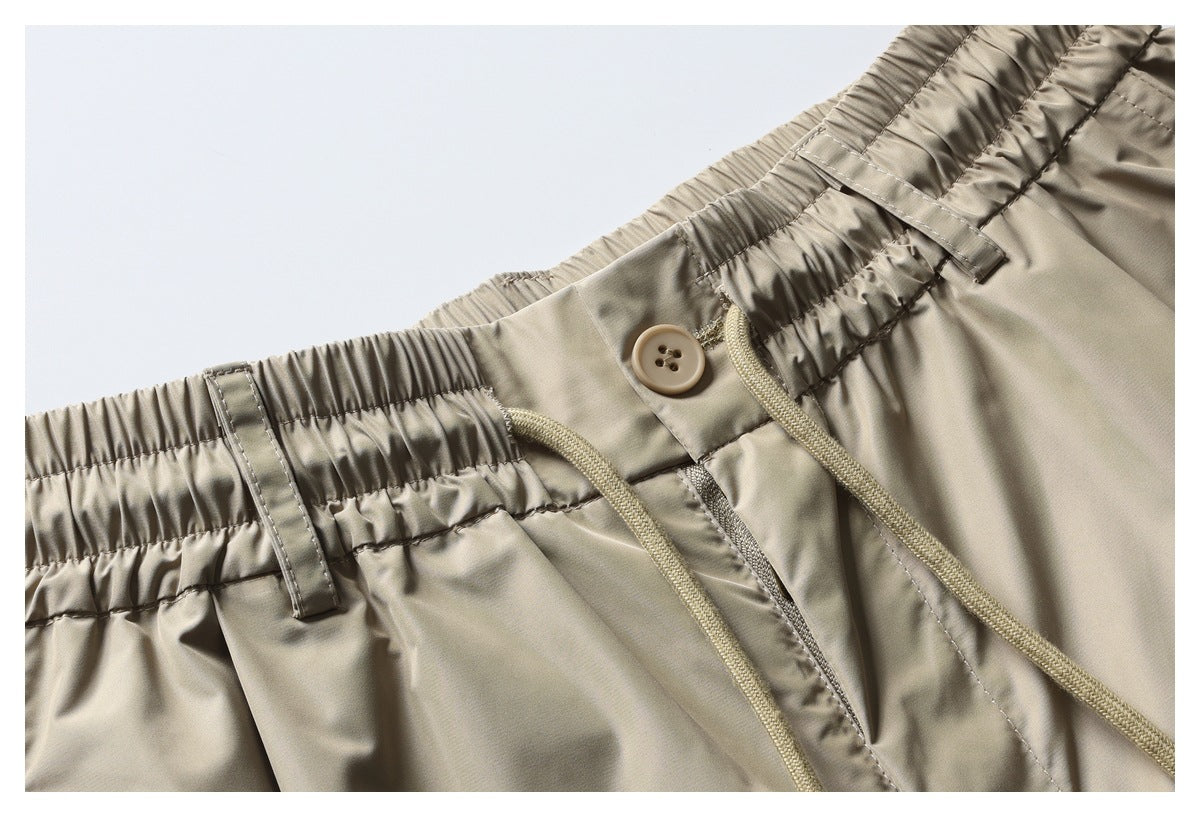 Close-up view of beige trousers showing the gathered waistband, button, belt loops, and drawstrings.