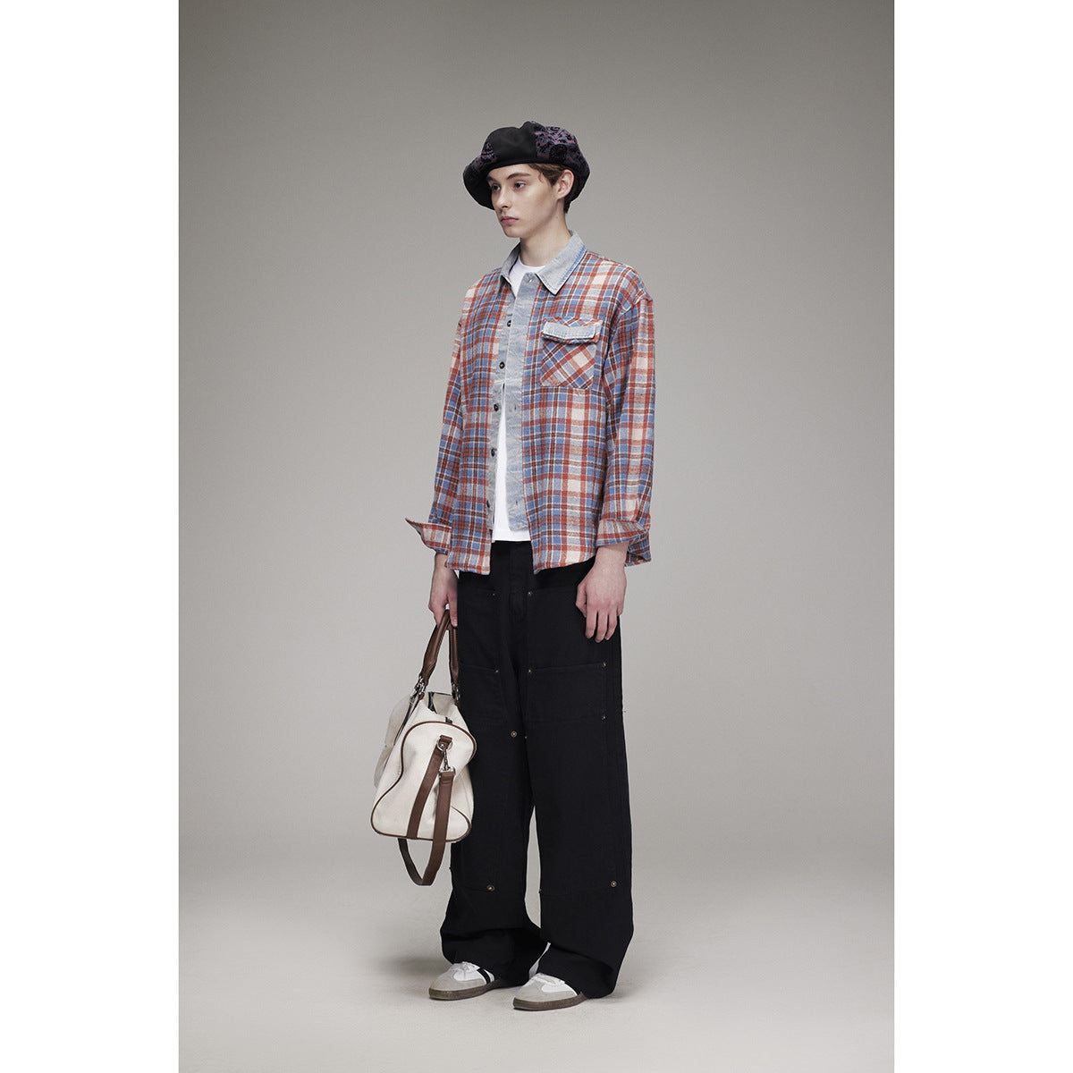 Full-length model wearing a blue, rust and cream plaid overshirt with black wide-leg trousers and a black patterned beret.