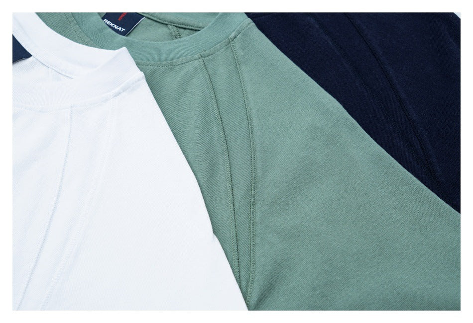 Close-up of white, sage green, and navy raglan crew-neck shirts arranged together.