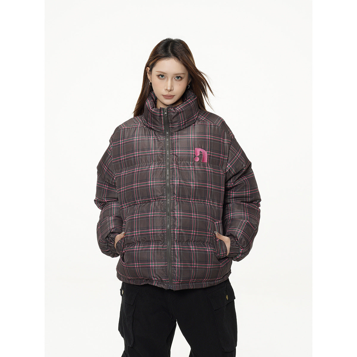 Model wearing a dark gray plaid puffer jacket with pink lines, a high collar, front zipper, and pink chest emblem.
