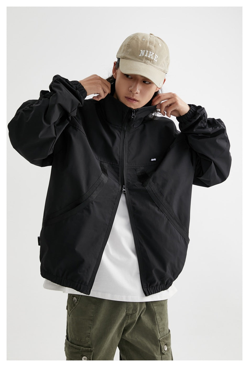 Front view of a model wearing a black zip-up jacket with curved pockets, a high collar, and elastic cuffs and hem.