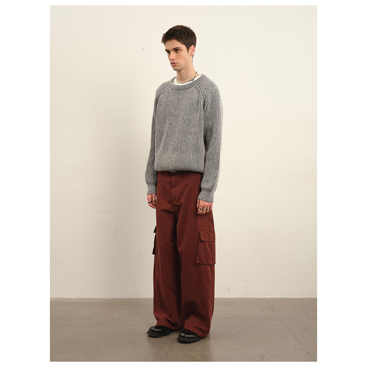 Model wearing a light gray ribbed crewneck sweater with raglan sleeves and rust-red cargo pants.