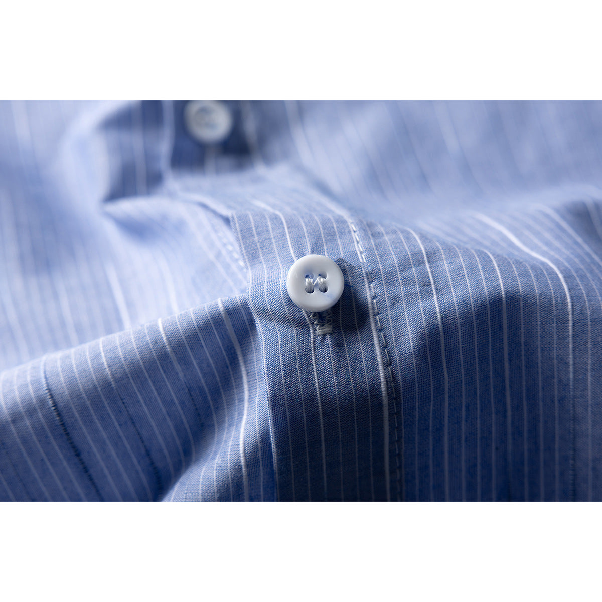 Close-up of a white button and stitching on blue-and-white pinstriped shirt fabric.