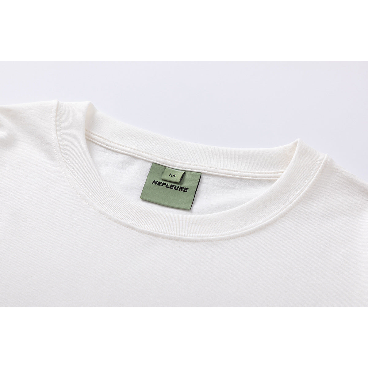 Close-up of a white T-shirt crew neck and sewn green NEPLEURE label marked M.