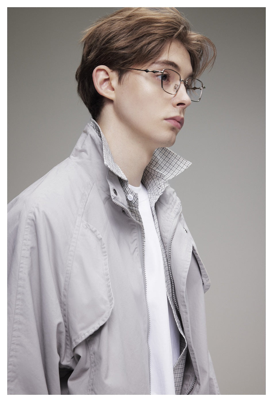 Close-up of a model wearing a light gray jacket with a high collar over a checked shirt and white tee.