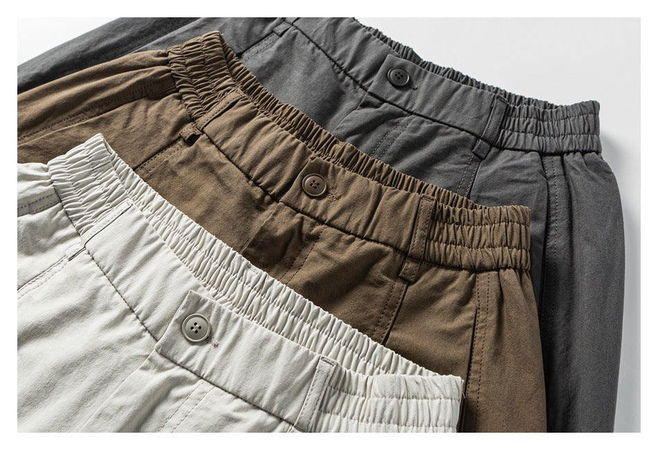 Close-up of the waistbands and button closures on the pants in pale gray-beige, brown, and charcoal.