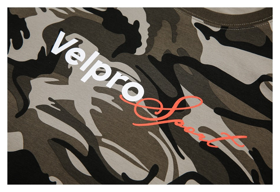 Close-up of white lettering and red script printed on a tan, brown, and black camouflage T-shirt.