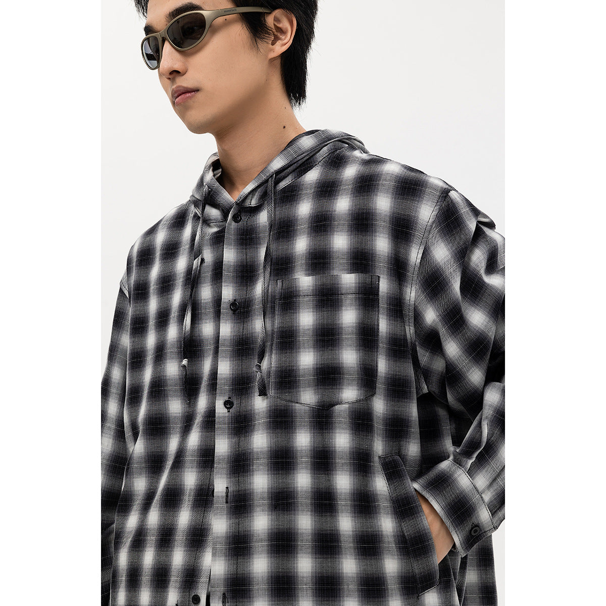 Close front view of a model wearing a black-and-white plaid hooded button-up shirt with a chest pocket.