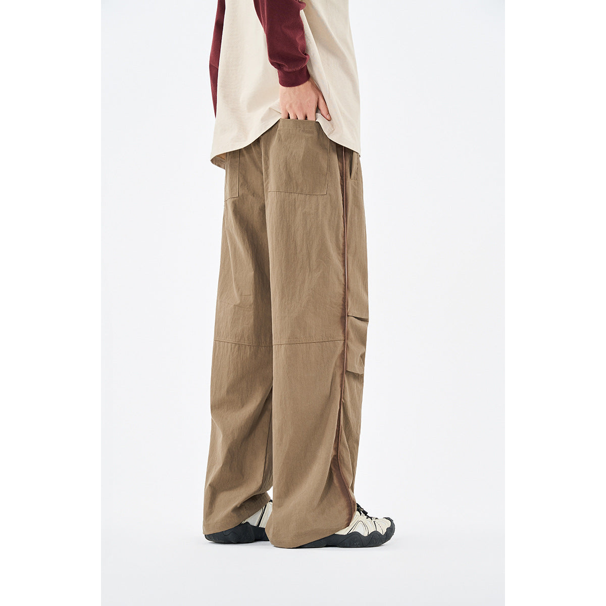 Rear angled view of a model wearing loose tan trousers with side piping and wide legs.