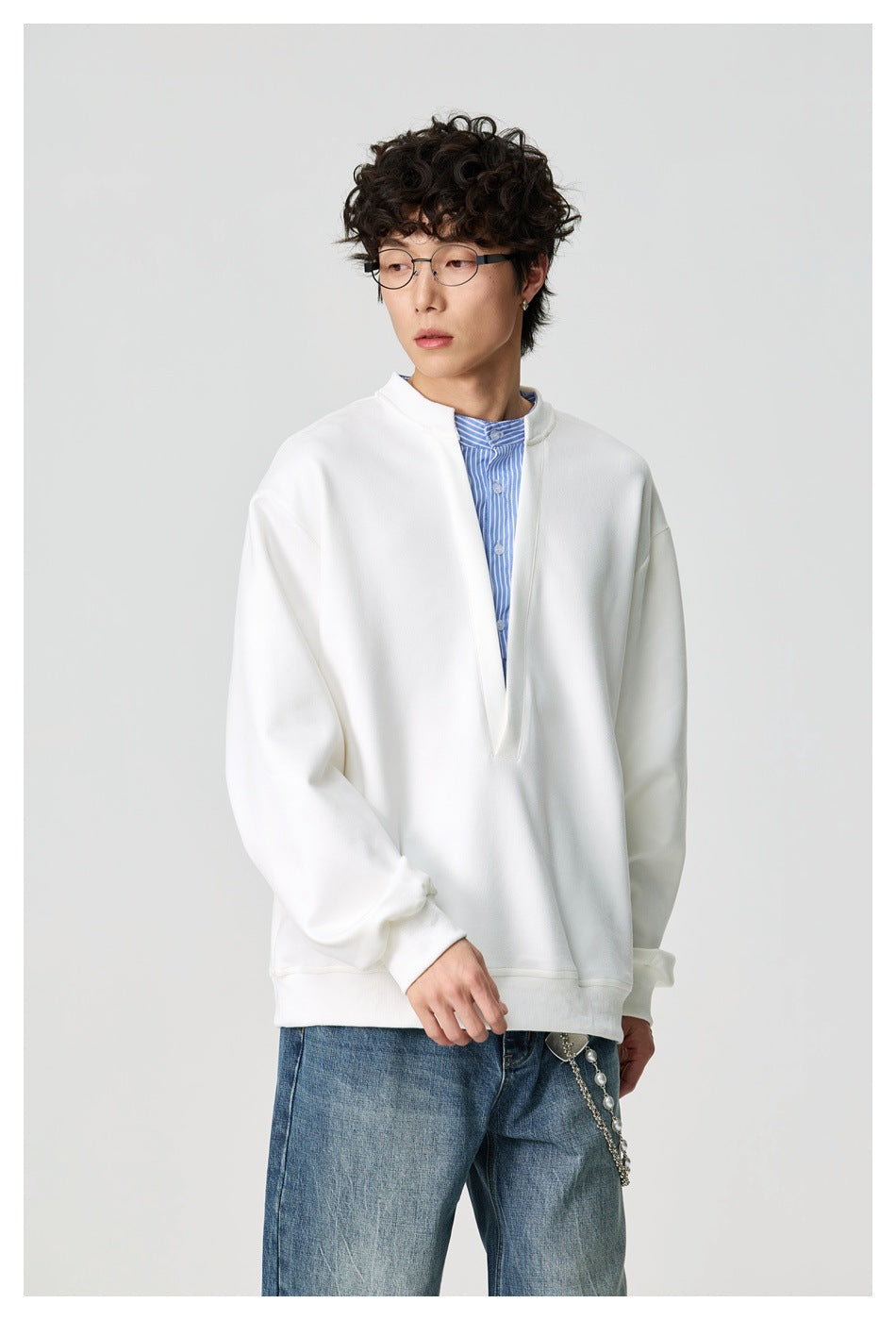Man wearing the white sweatshirt with striped shirt insert at the V neckline, styled with blue jeans