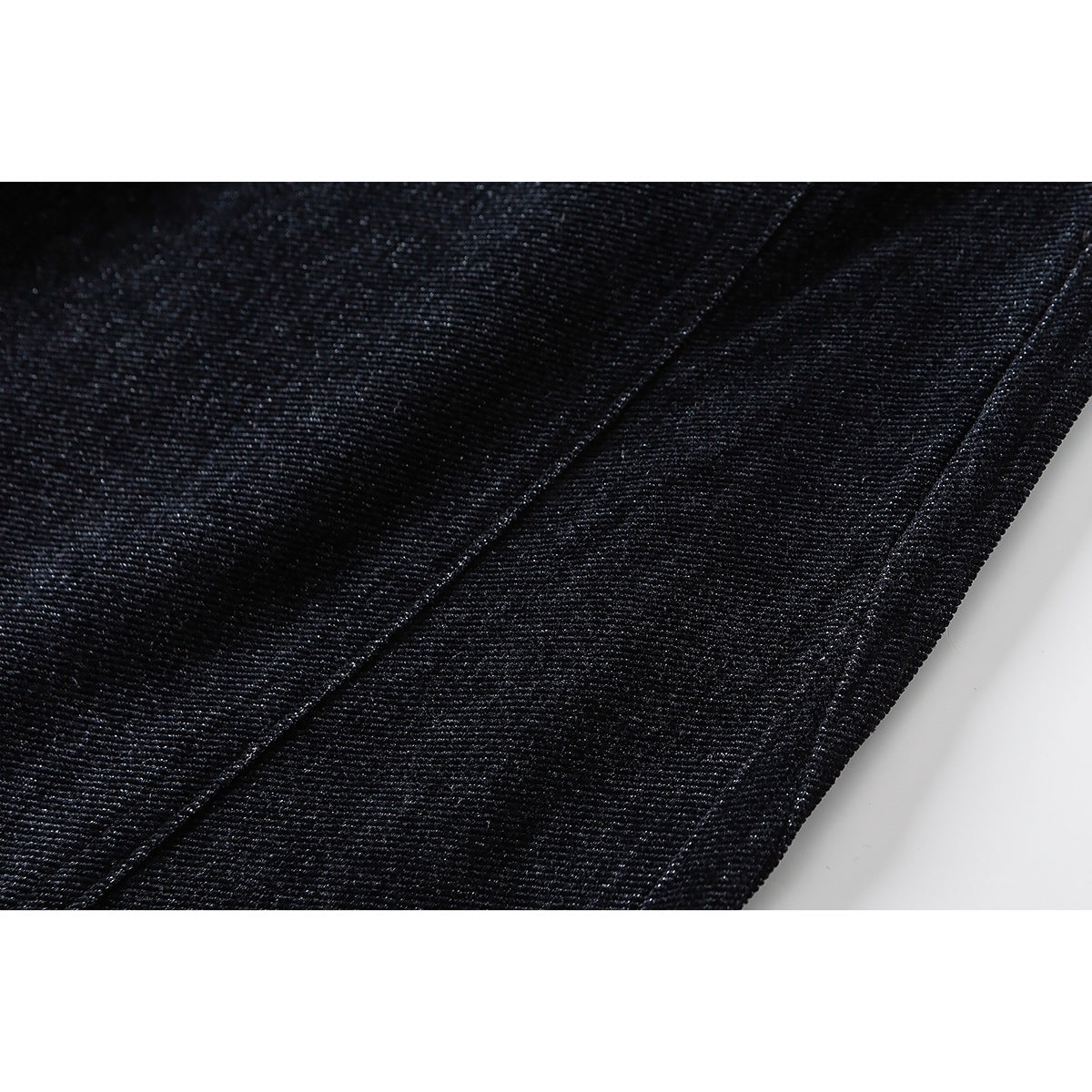 Close-up of dark textured pants fabric with a diagonal seam and finished edge.