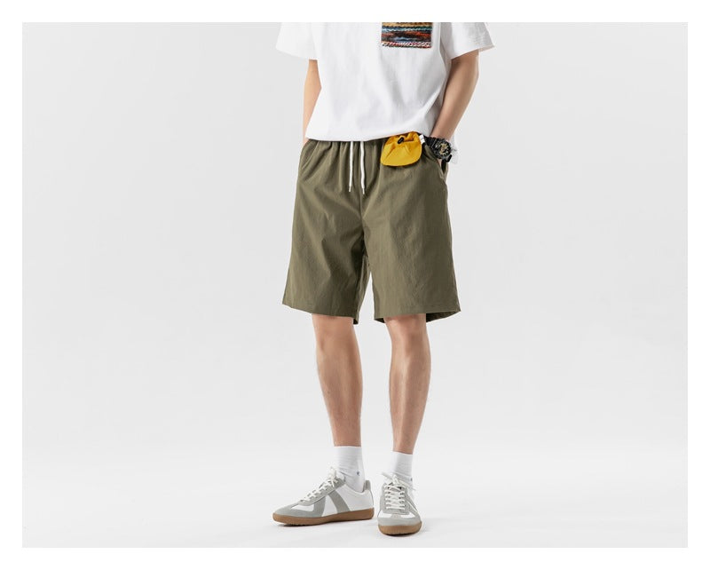 Front view of a model wearing olive drawstring shorts with a small yellow pouch at the waistband.