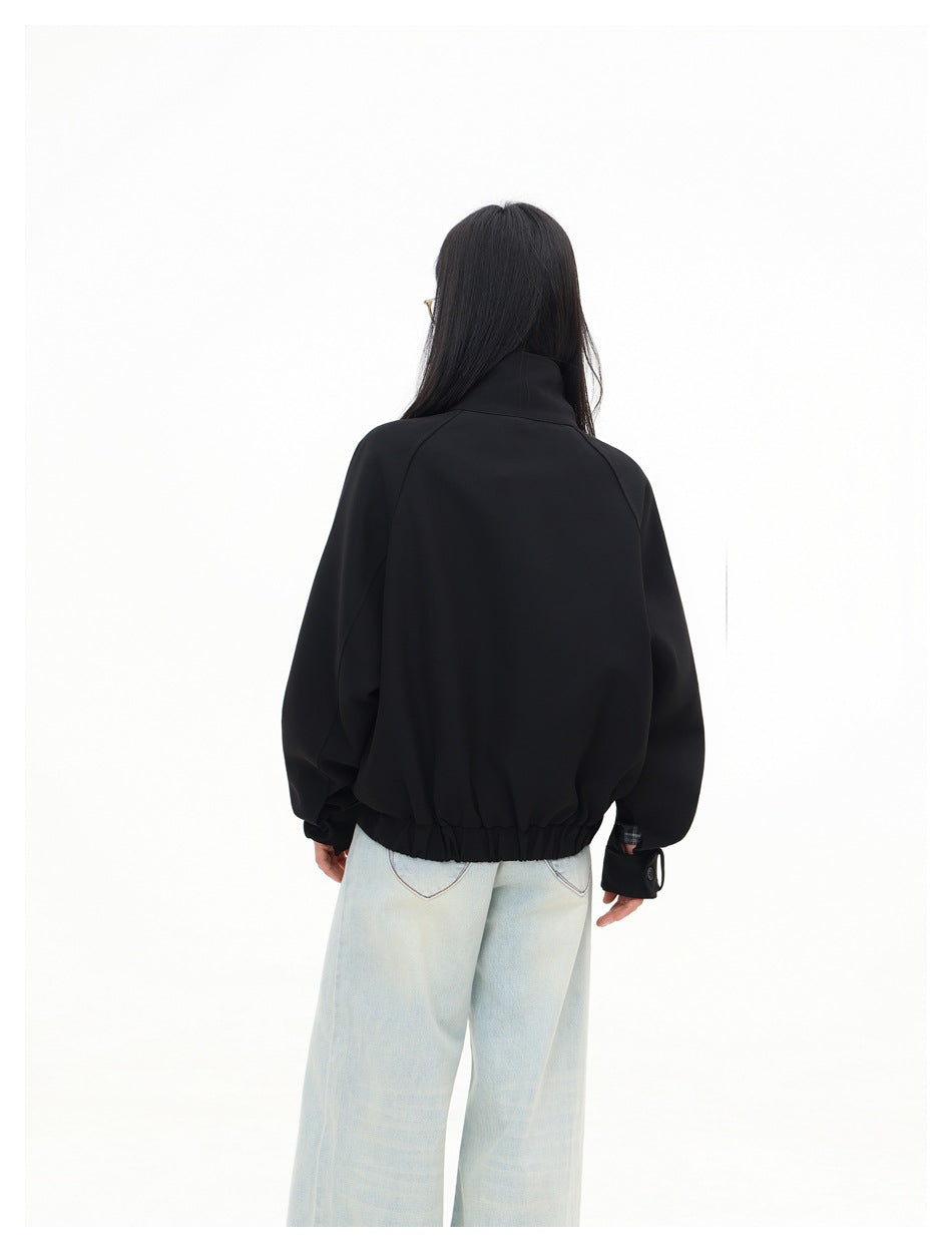 Rear view of a model wearing a black jacket with raglan sleeves, buttoned cuffs, and a gathered hem.