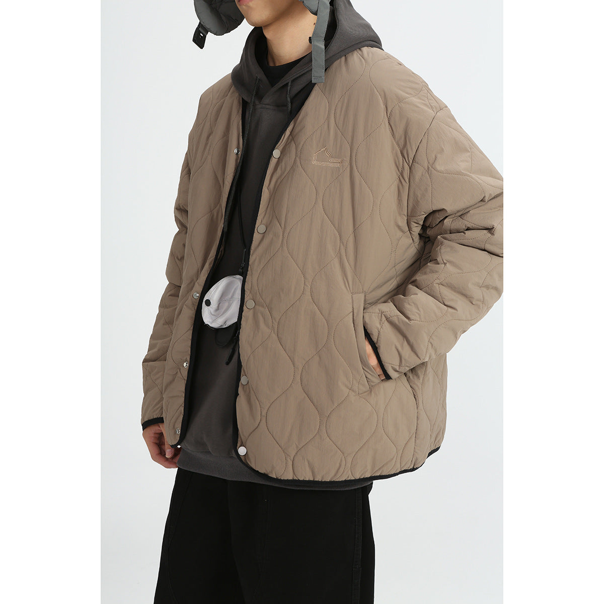 Model wearing a taupe quilted jacket with a snap front, black trim, side pockets and a hooded layer underneath.