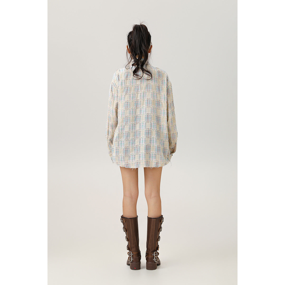 Back view of a model wearing a cream pastel-plaid oversized shirt with a curved hem.