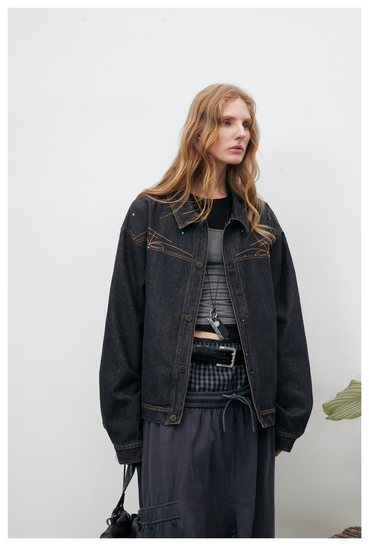 Close-up of a model wearing a washed black denim jacket with embroidered chest yoke over a gray top and a plaid layered skirt