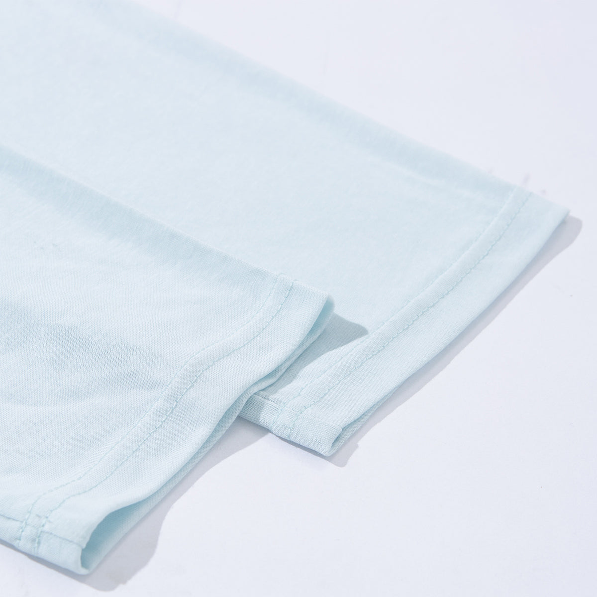 Close-up of the stitched hem and folded edge of a pale blue shirt.