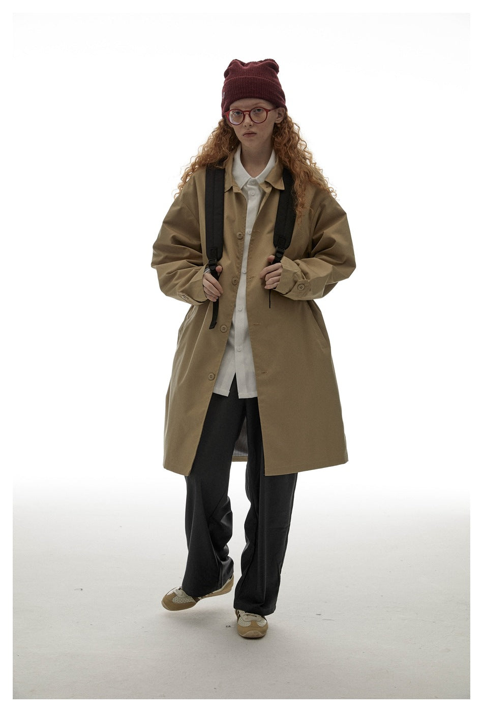 Model walking in an oversized tan button-front coat with a pointed collar and cuff tabs.