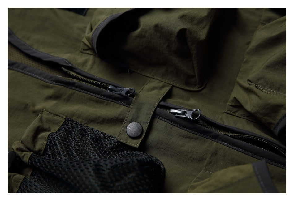 Close-up of an olive-green garment's front zipper, snap tab, and black mesh pocket.