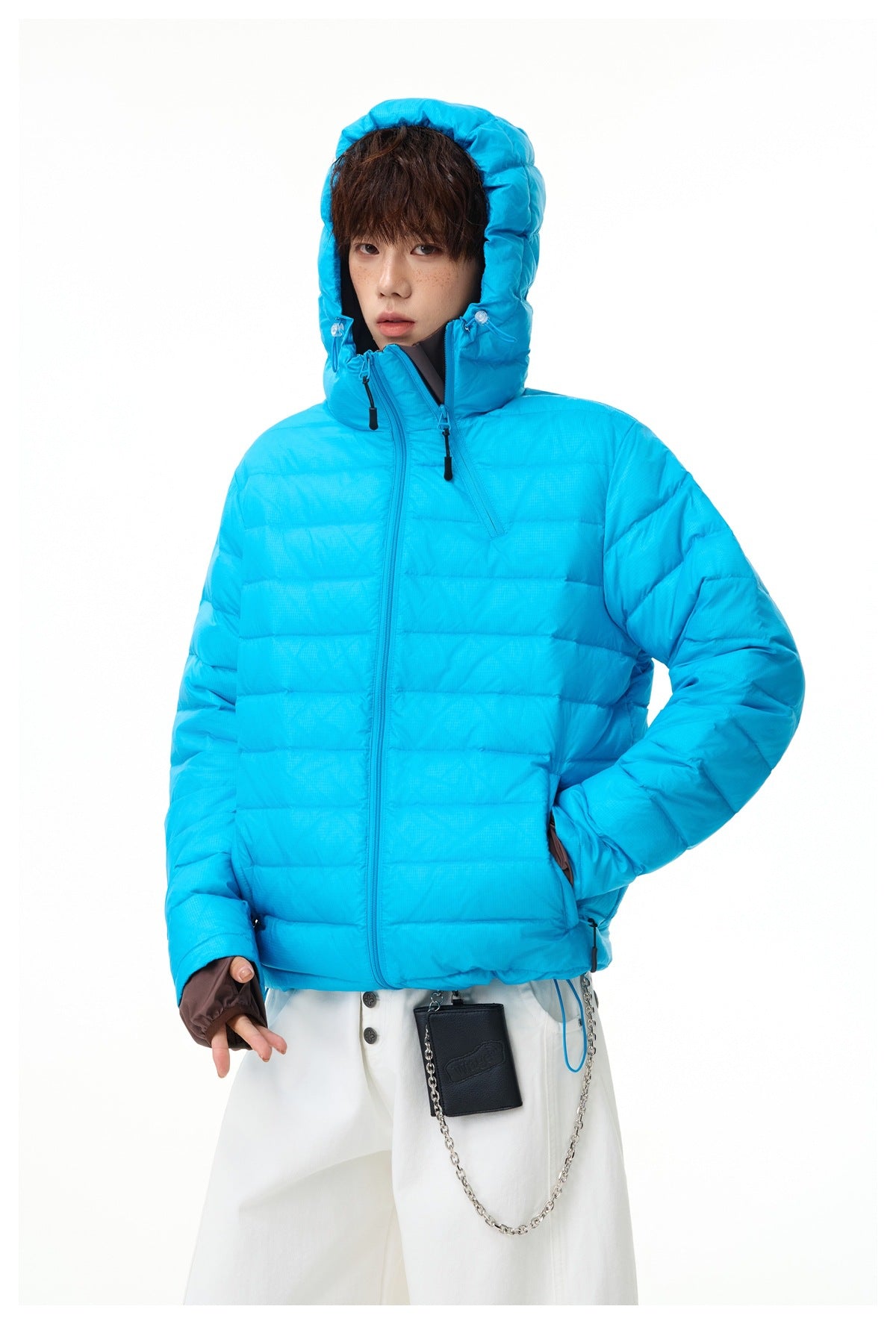 Front view of a model wearing a bright cyan quilted jacket with a raised hood, high collar and front zipper.
