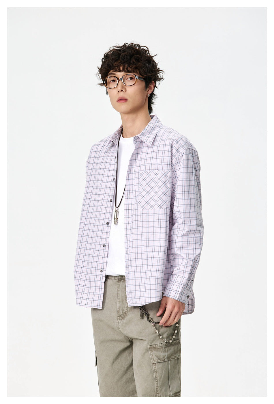 Model wearing an oversized pale pink plaid button-up shirt open over a white tee, shown at a three-quarter angle.