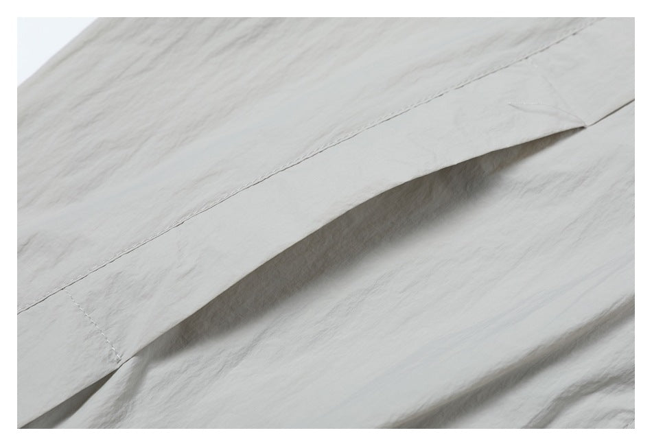 Close-up of a stitched seam and folded edge on light gray jacket fabric.