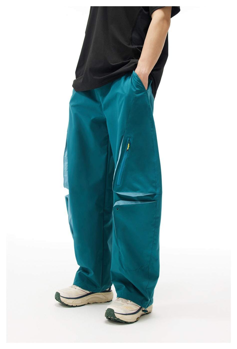 Side view of teal cargo pants worn with large flap thigh pockets, zip closures, and roomy legs.