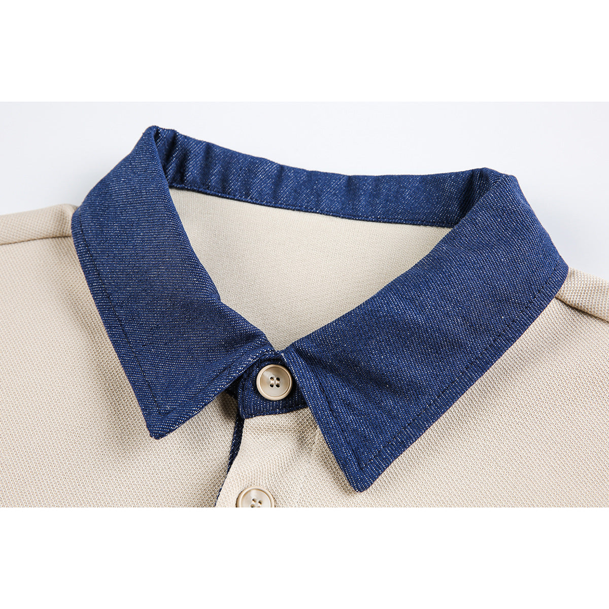 Close-up of a cream shirt with a dark navy pointed collar and beige buttons.