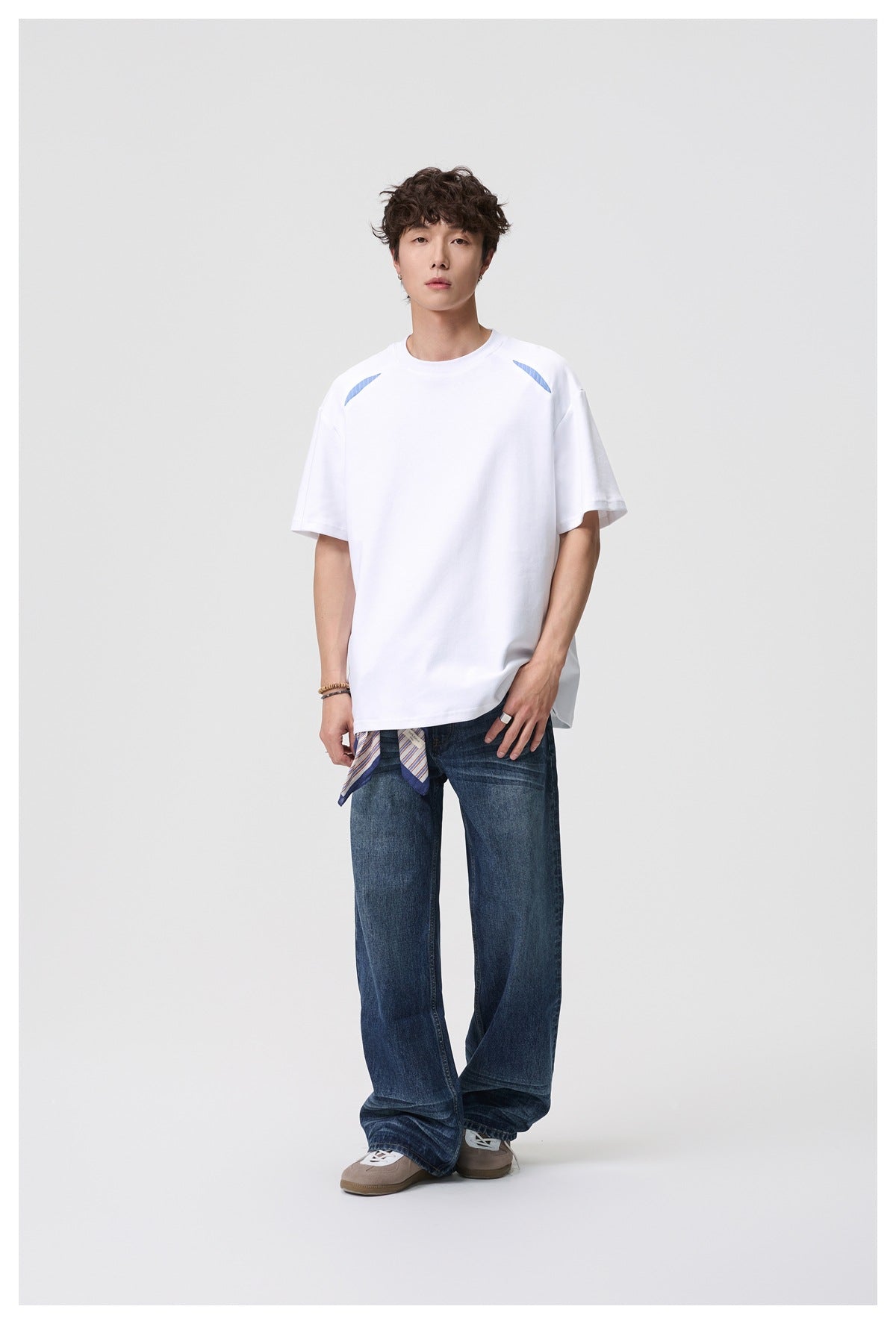 Full-length front view of a model wearing a white oversized T-shirt with blue shoulder accents and loose blue jeans.