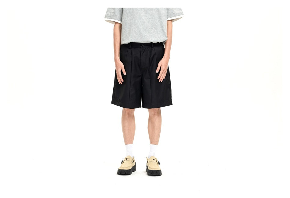 Front view of a model wearing black pleated shorts with a gray T-shirt and beige shoes.