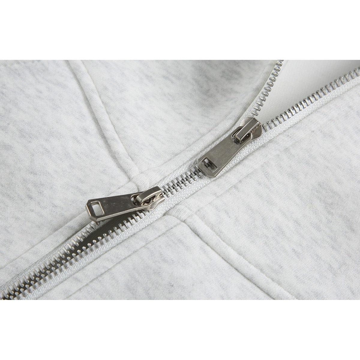 Close-up of the light gray heather hoodie’s silver two-way zipper and surrounding seams.