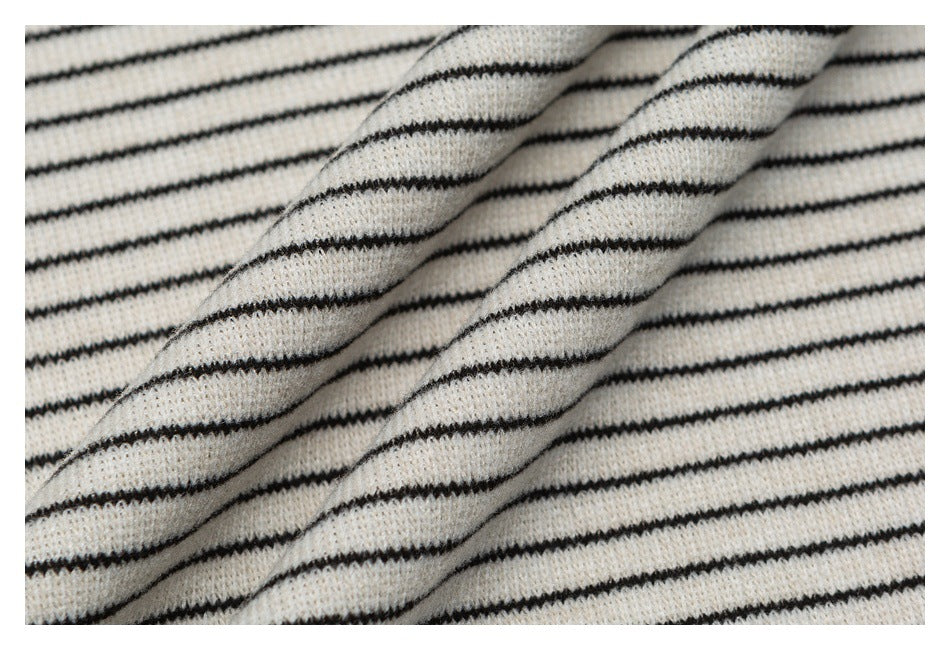 Close-up of cream fabric with narrow black stripes draped in soft folds, showing its knit texture.