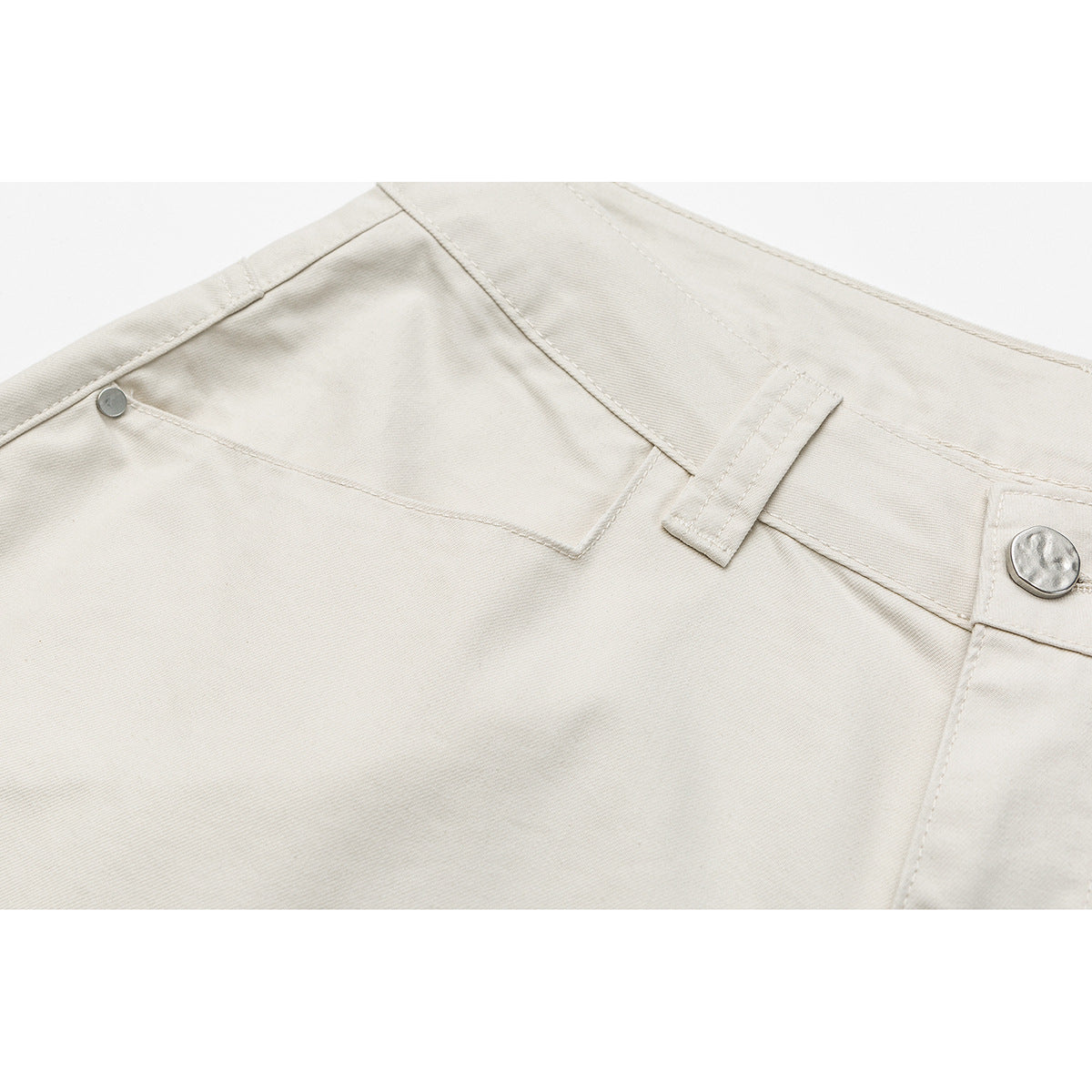 Close-up of cream shorts showing the waistband, belt loop, metal button and front pocket details.