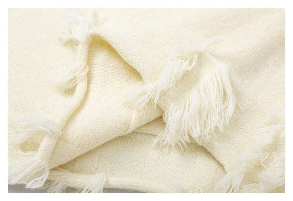 Close-up of cream knit fabric with several long fringe tassels.