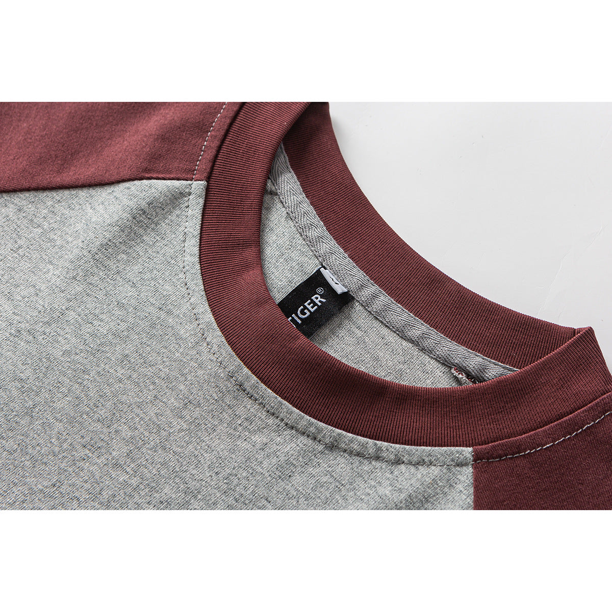 Close-up of a gray and burgundy raglan T-shirt neckline, ribbed collar, stitching, and inner label.