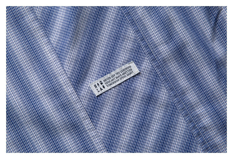 Close-up of a small sewn English-text label on blue-and-white checked shirt fabric.